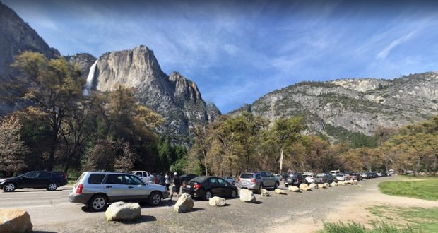 Vehicles parked in lot by Yosemite Falls waterfall, nature in background.