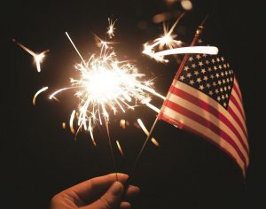 Image of an American flag next to a fireworks sparkler.