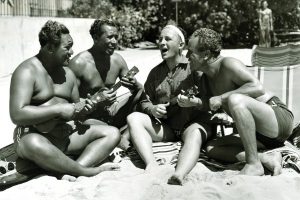 Image of Bing Crosby singing with the locals on the beach in front of the Royal Hawaiian.