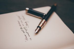 Image of a poem on a piece of paper with a pen resting on it. 
