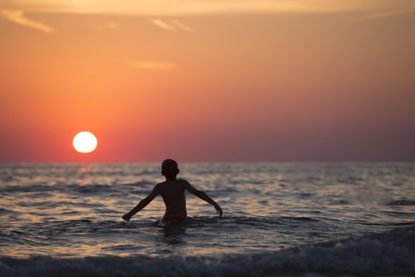 Image of a boy splashing in the water at sunset. 