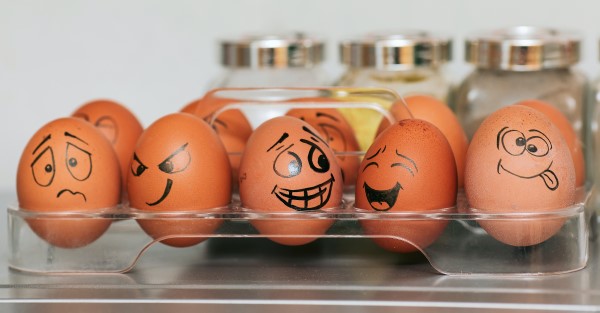 Image of a dozen eggs with funny faces drawn on them. 