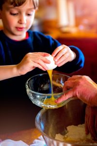 Image of a young boy cracking an egg into a bowl. 