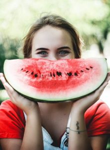 Image of a woman holding up a large slice of watermelon. 