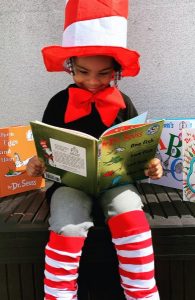 Image of a young child dressed up like the Cat in the Hat reading a book. 