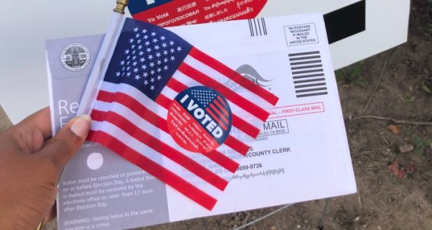 Image of a hand holding a voting ballot and an American flag.