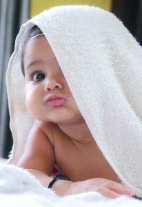 Image of a baby peeking out from under a blanket. 