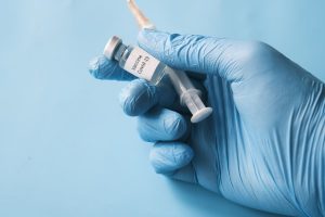 Image of a gloved hand holding a COVID-19 vaccine in a syringe.
