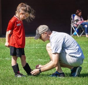 Image of a father tying a young girl's shoelaces before a soccer game. 
