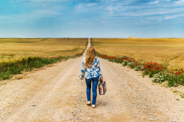 Image of a young girl walking down a dirt road with a suitcase.