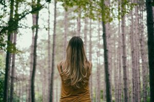Image of a woman standing alone in a forest with her back to the camera. 