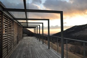 Image of a wooden deck overlooking a mountain with the sun setting in the background. 