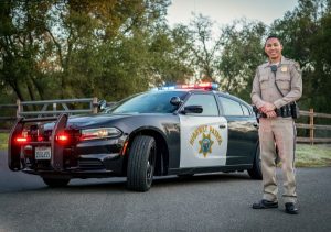 Image of a CHP officer in front of his patrol car. 