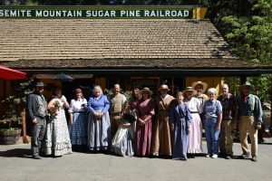 Image of a large group of people dressed in vintage clothing in front of a railroad station. 