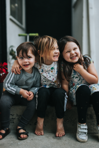 Image of three children sitting on a step laughing and hugging.