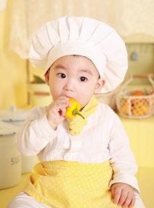 Image of a small child in a chef's outfit eating a yellow bell pepper. 