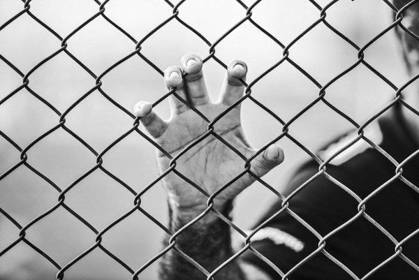 Image of a prison inmate with their hand on the fence. 