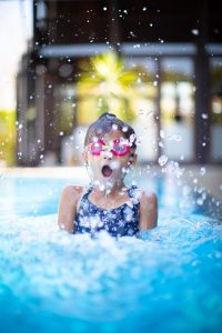 Image of a young girl popping up out of a swimming pool. 