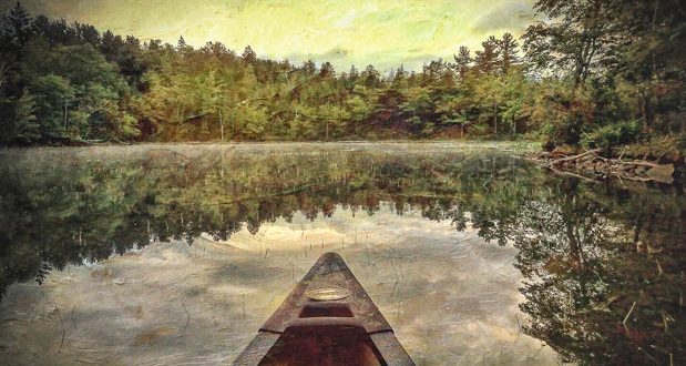 Image of someones view of being in a canoe on a lake with the reflection of the trees