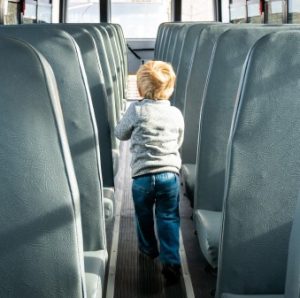 Image of a little boy walking down a school bus aisle. 