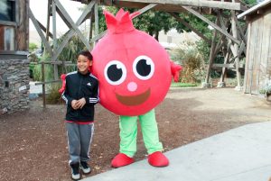Image of a kid next to a pomegranate mascot