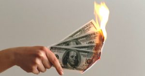 Image of a handing holding hundred dollar bills on fire.