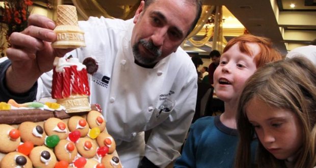 Image of a chef helping two small children build gingerbread house.