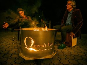 Image of two men sitting besides a fire pit drinking wine.