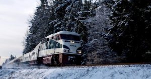Image of an Amtrak train rolling through a snow-covered forest.