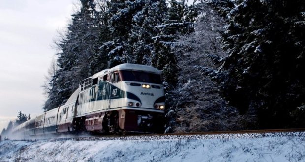 Image of an Amtrak train rolling through a snow-covered forest.