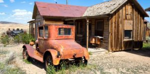 Image of an old car next to an old building out in the middle of nowhere