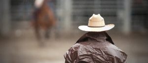 Image of a cowboy watching a horseback rider in the rain.