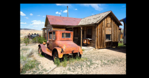 Image of an old, abandoned car in front of a ghost town.