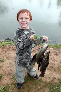 Image of a young boy holding up a bunch of fish that he just caught.