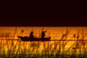 Image of people fishing in a boat at sunset. 