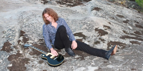 Picture of Erick Tyler on a rock looking at his guitar