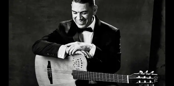 Black and white picture of Mikel Soria dressed up in a tuxedo with a bowtie and his guitar