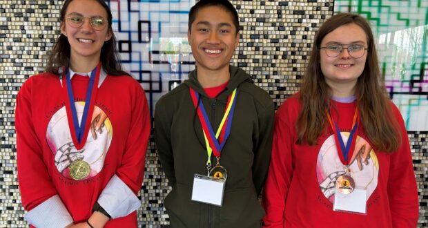 1. Three students proudly wearing medals, standing in front of a wall.