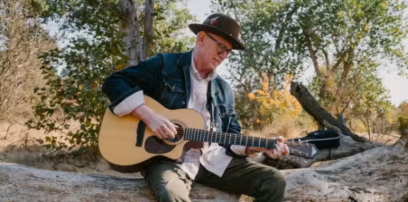 image of Randy Freeman playing the guitar on a fallen tree