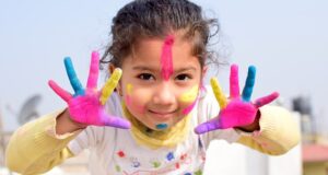 A child with painted hands and face, expressing joy and imagination through art.